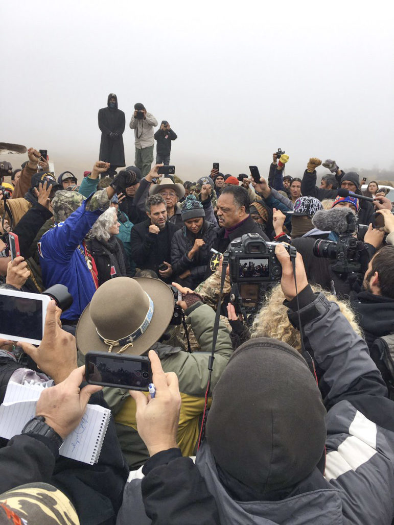 Reporters, protesters and everyone in between swarms around the Rev. Jesse Jackson on the highway near camp. Whether a traditional journalist or an activist reporter, you need a press pass to access camp and cover protest activities without hassle.