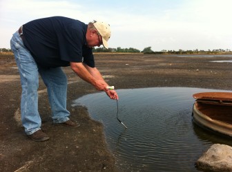 Daryl Peterson tests the water at the site of a saltwater spill with his electro conductivity meter, which will tell him how much salt is in the water.