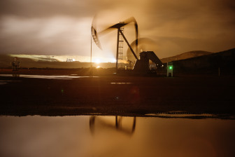 A pumpjack works throughout the night, bathed in the light from flares and electric lights on oil well pads near Watford City, North Dakota, which also illuminate low-hanging clouds.